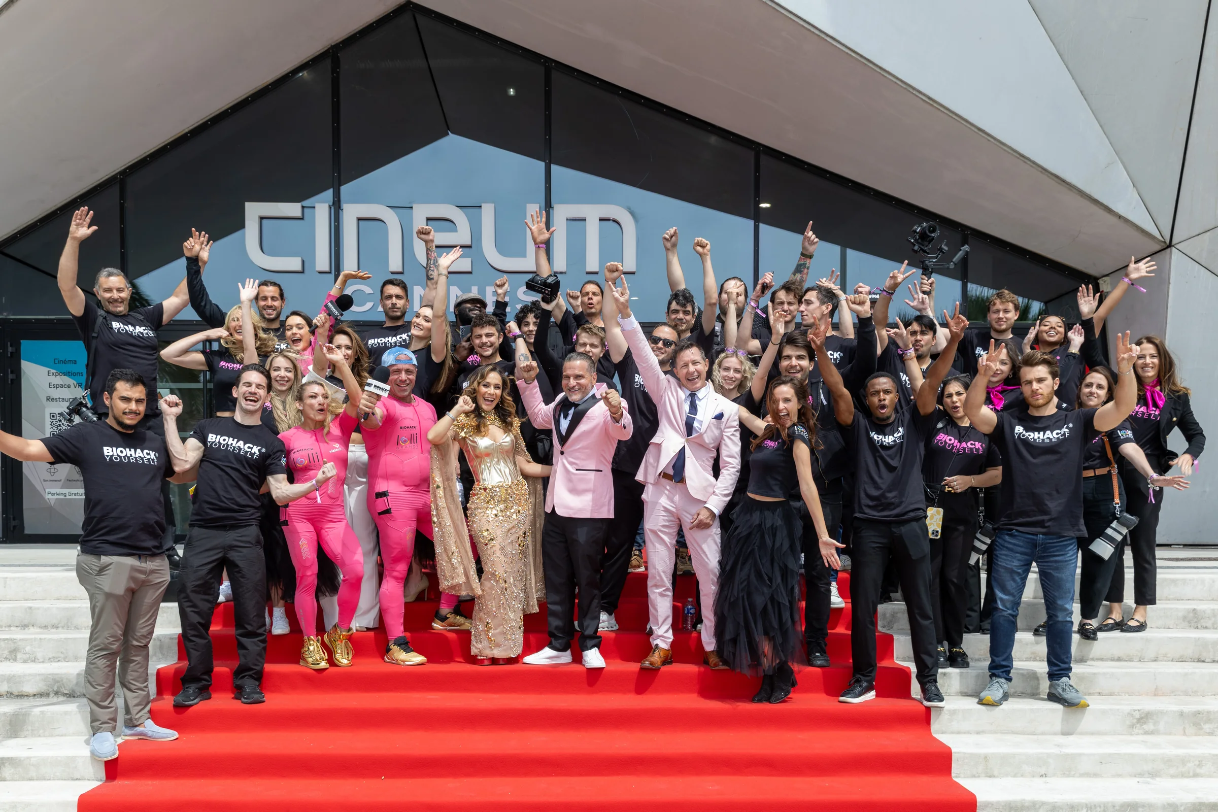 More than forty cast and crew members, most in studio shirts and several holding cameras, cheering on the red-carpeted steps of Cineum Cannes